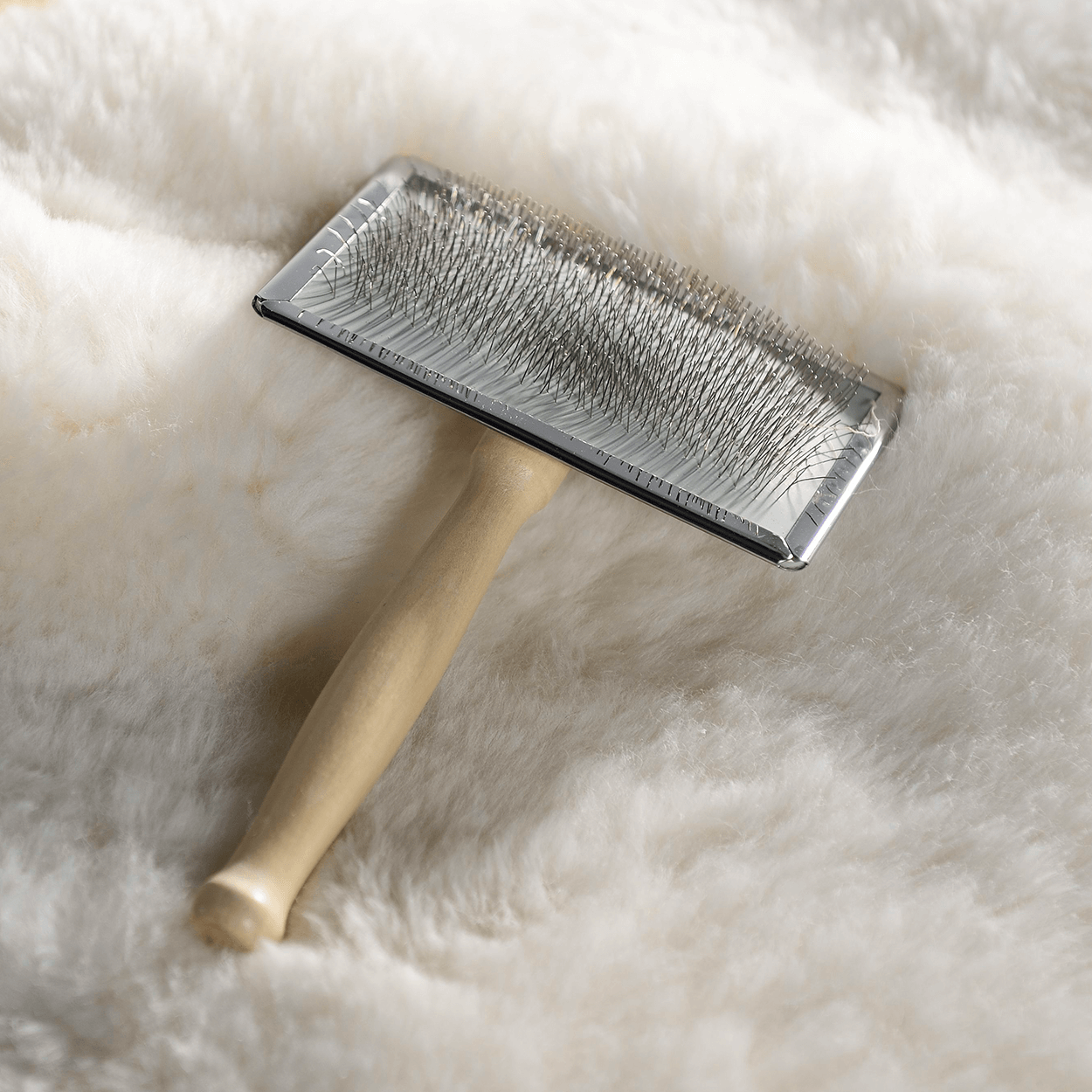 Fellpflegebürste liegt auf kuscheligem weißen Schaffell.